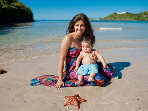 A mom sits in the sand with her son in Antigua. The toddler is looking at a large starfish.