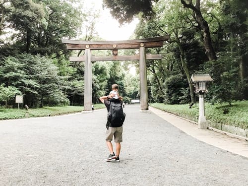 A dad holds his young daughter on his shoulders while they walk through Meiji Shrine in Tokyo, Japan.