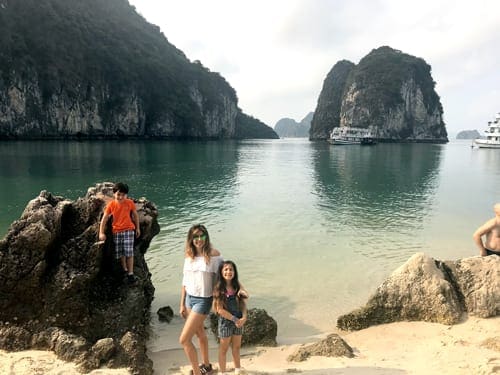 A mom and her two kids stand together in Ha Long Bay with the water behind them.
