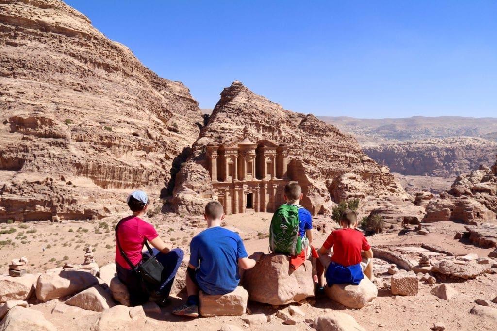 A mom and her three sons sit along the rocks looking out onto a historic sight in Petra.