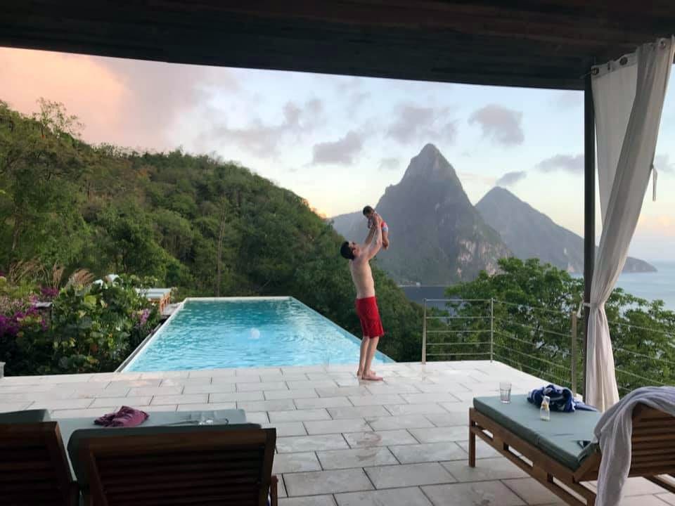 Father holding baby daughter in the air by pool overlooking St. Lucia.