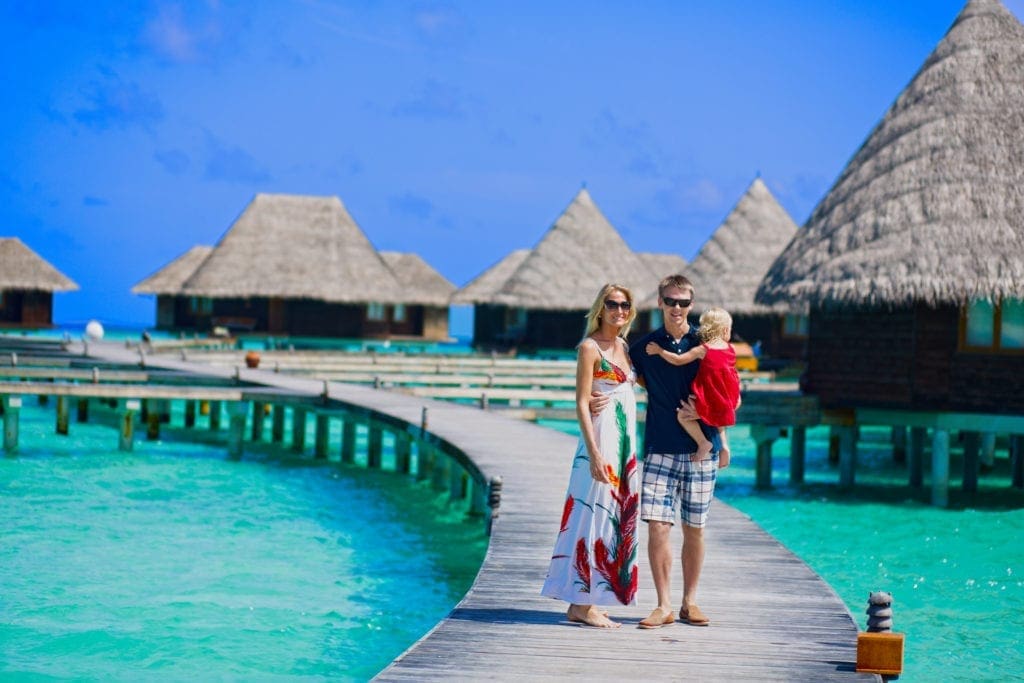 Family of three walking on the bridge towards to water bungalows on Maldives.