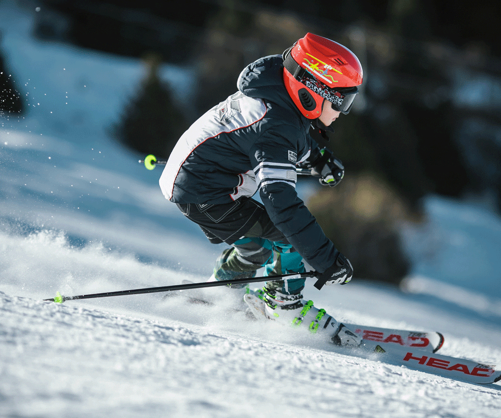 Boy skiing with red helmet while on a vacation for family skiing in Alpendorf.