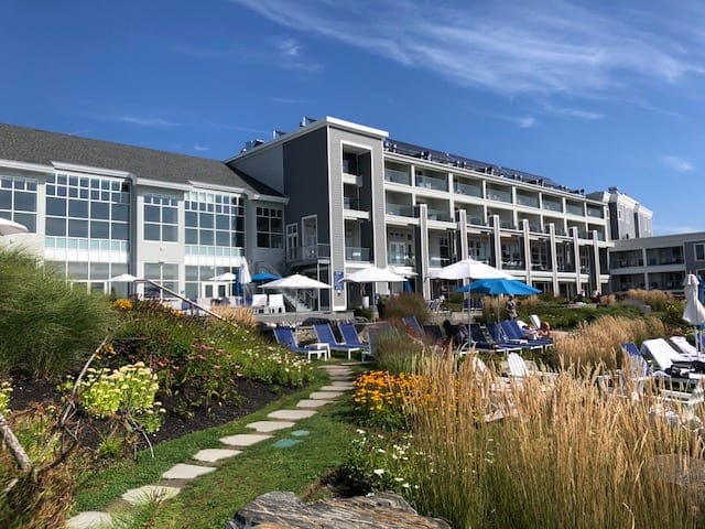 The rear exterior of Cliff House in Maine, featuring a lovely rock path leading to the ocean and blue skies.