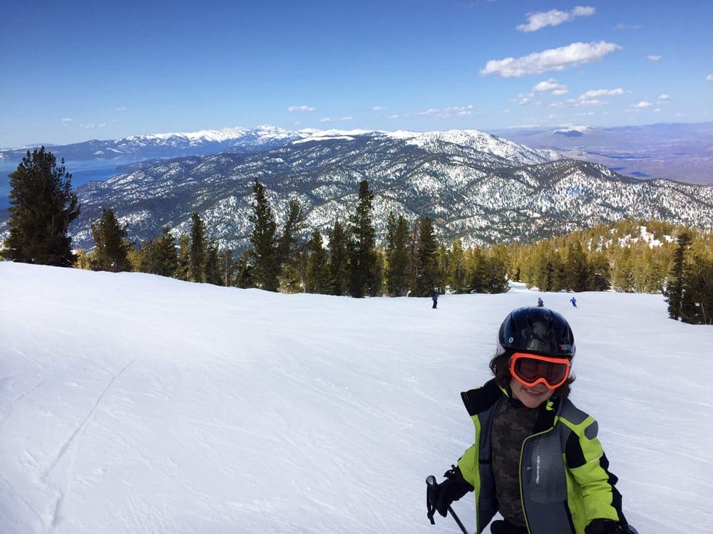 A boy wearing a green ski jacket skiing on a slope at Heavenly Resort, one of the best ski resorts near Lake Tahoe for families.