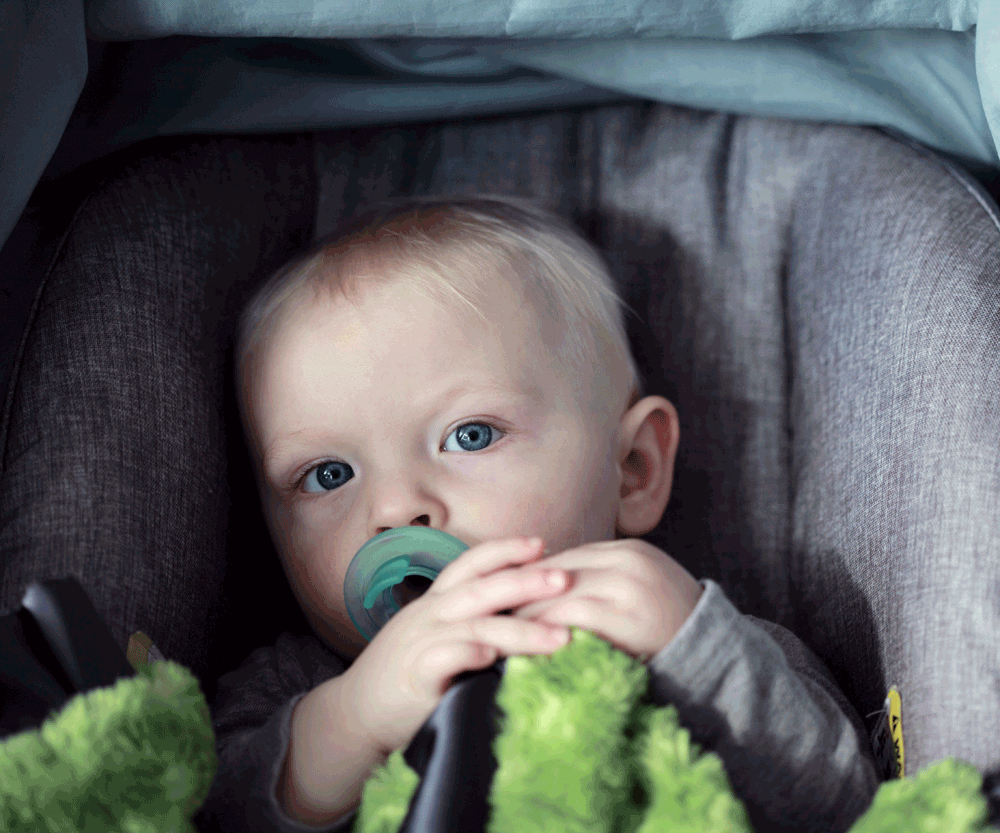 Baby with blue eyes and pacifier sitting in carseat