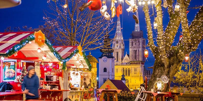 People enjoy the Advent Zagreb at Strossmayer Promenade, featuring Christmas stalls and bright light.