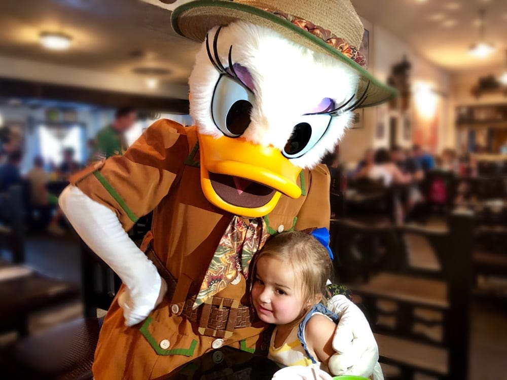 A young girl hugs Daisy Duck dressed in a safari costume.