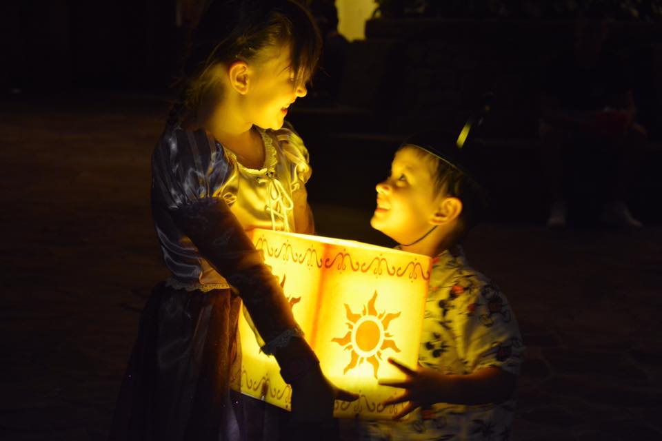 Two young kids look at eachother smiling while holding a Rapunzel-inspired lantern at Walt Disney World.