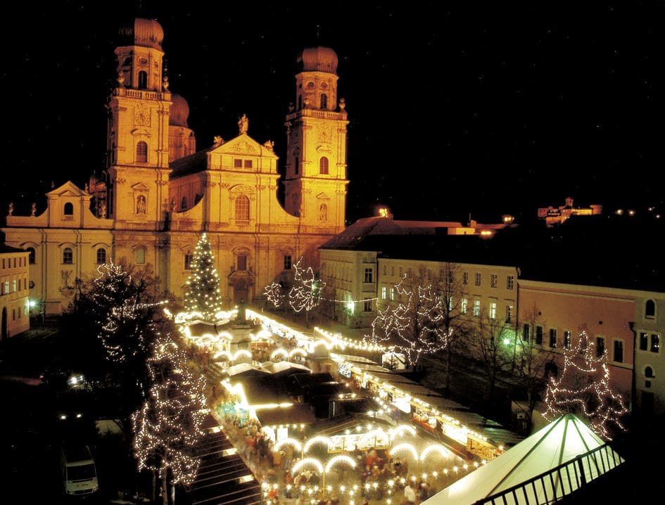 A large square in front of a church is covered in twinkling lights for the Passau Christmas Market.