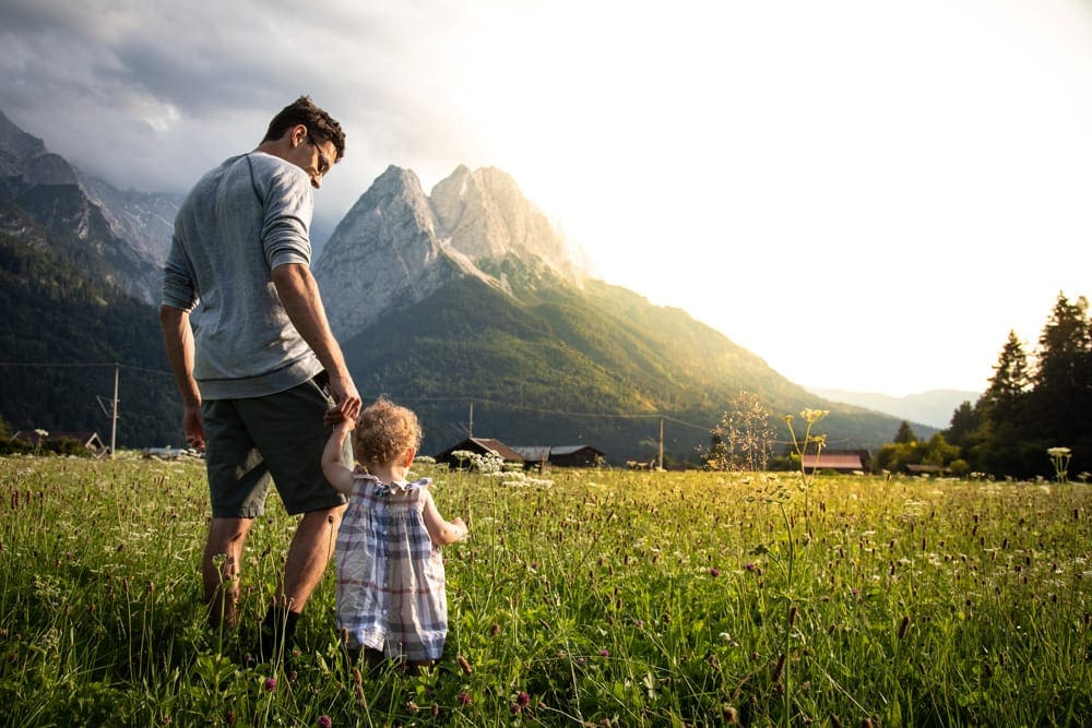 Father holding hands of her little daughter and walking in th lush green  landscape 