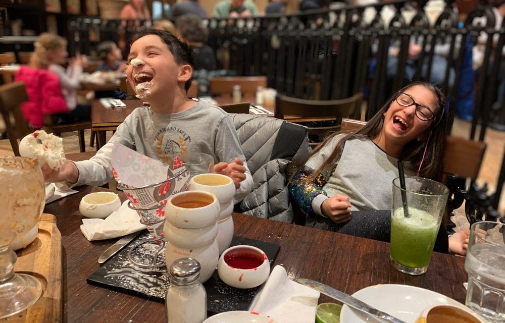 Two kids laugh, one with whipped cream on his nose, while enjoying dinner at Max Brenner's, one of the most unique New York City restaurants with Kids.