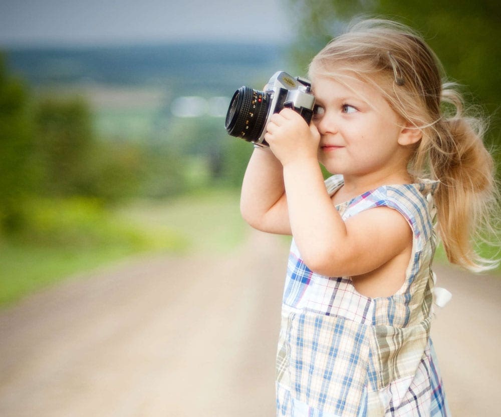 Young girl in dress taking a picture with a professional camera, one of the best outdoor gifts for families.