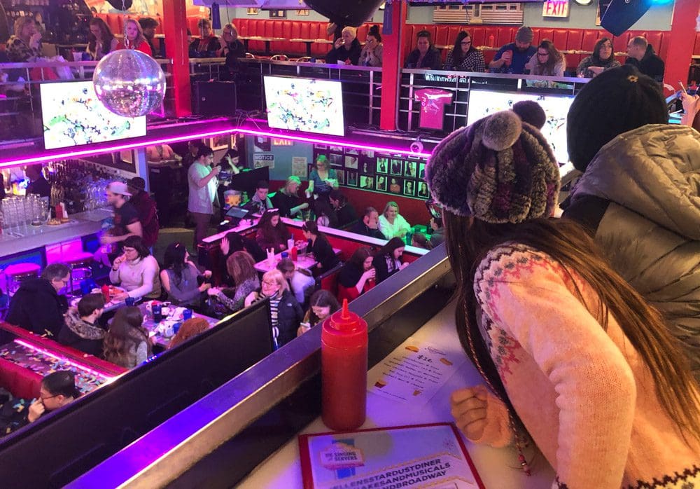 Two kids look over the railing onto the floor below, filled with other diners, at the Stardust Diner in NYC, one of the most unique New York City restaurants with Kids.