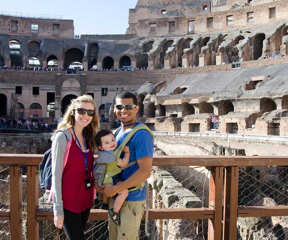 Two parents with their baby in carrier stand inside the Colosseum in Rome, one of the best spring break destinations for families around the world.