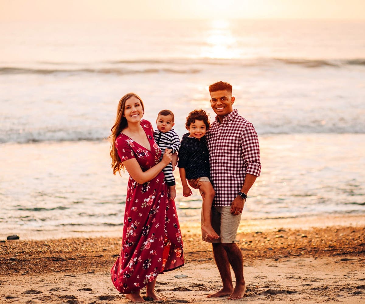 A family of four stands together on a beach in Southern California at sunset.