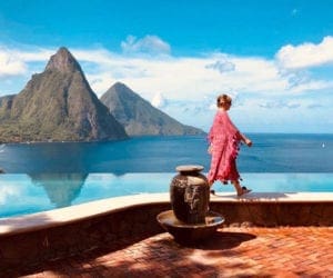 A woman walks along an edge of a hotel terrace with the St. Lucia mountains and ocean in the distance.