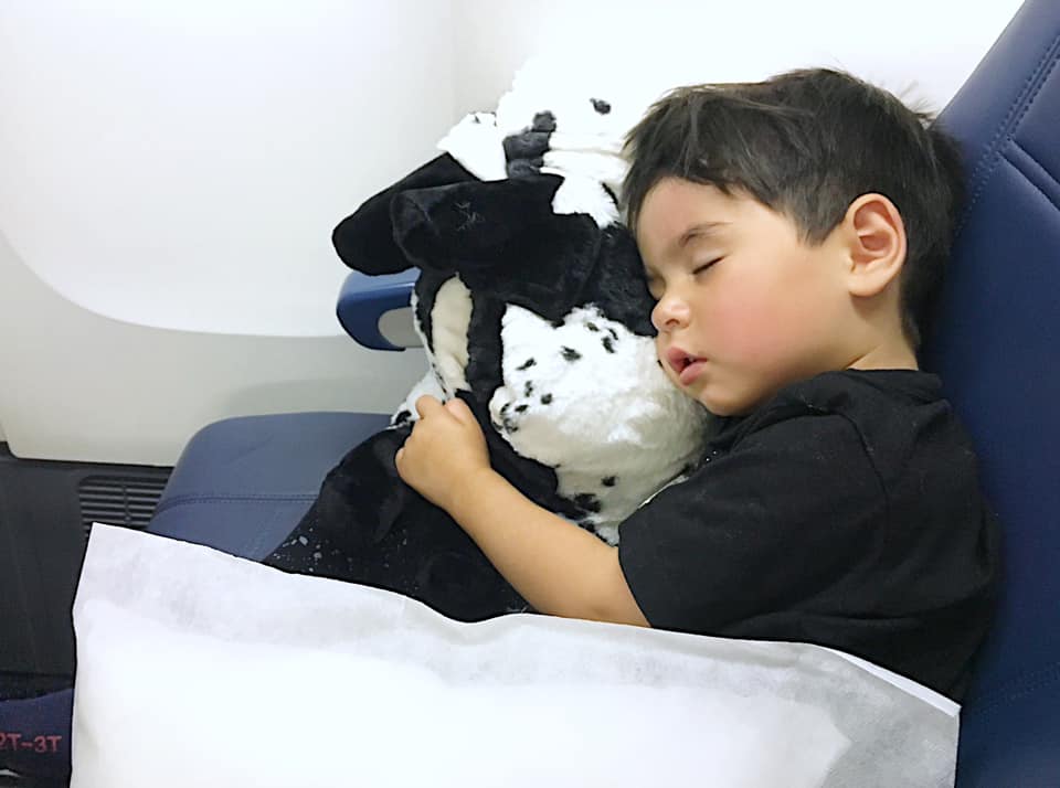 Little boy sleeping with a in the plane. Maintaining a good sleep routine is one of the best tips for traveling with a toddler.