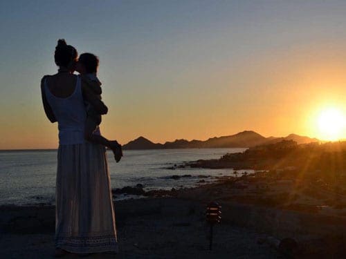 At sunset, a mom holds her small child on a beach in Los Cabos.