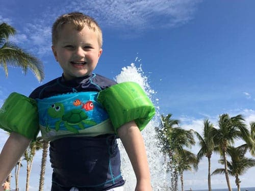 A young boy wearing swim wings stands in a pool in Cabo.