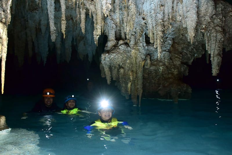 Family with flashlights swimming in Rio Secreto underground cave, perfect while exploring Cancun with kids.