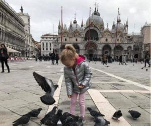 Young girl in silver jacket feeding pigeons at St Marks Basilica Venice Italy