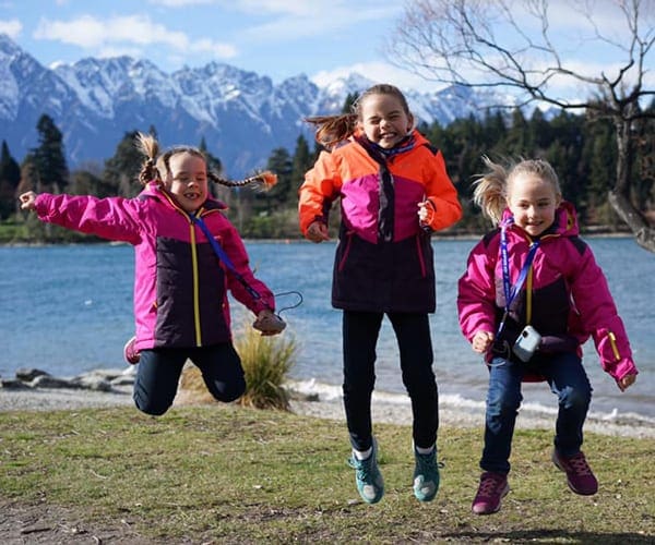 Three girls in pink jackets jumping up and down while hiking in New Zealand.