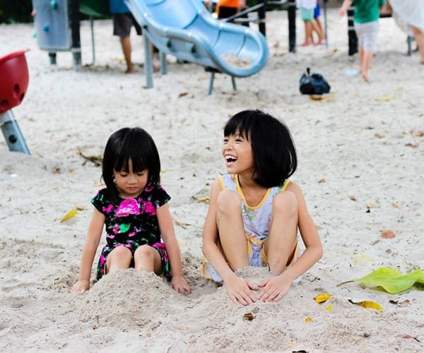 Sisters sitting in sand at playground in Singapore