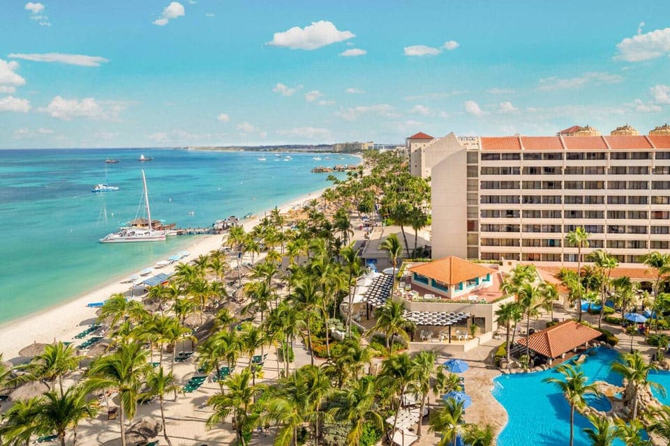 Aerial view of Barceló Aruba,one of the best family resorts in Aruba, featuring a blue pool, green palms, and large buildings.