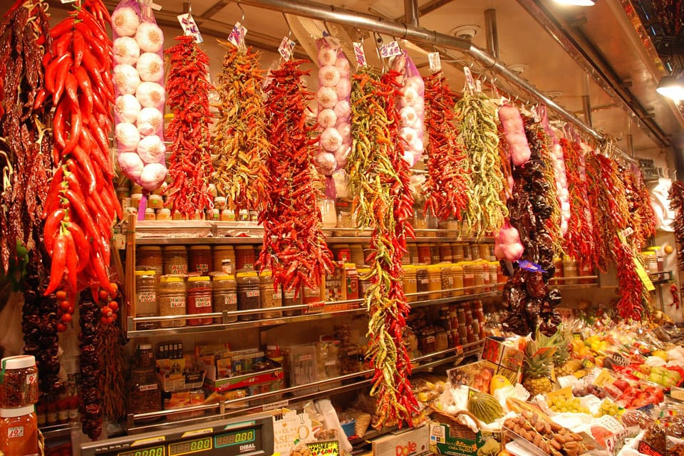 Several strings of peppers and garlic hang from a stall at the Boqueria Market.