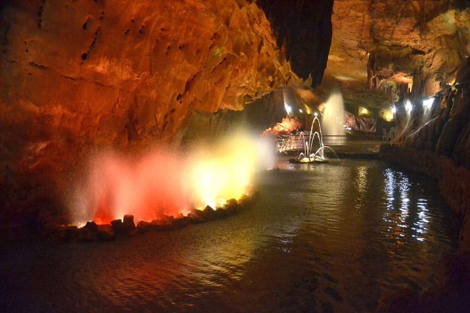 Inside the Caves of Grutas de Mira de Aire, featuring red and yellow lights, water, and a cave setting.