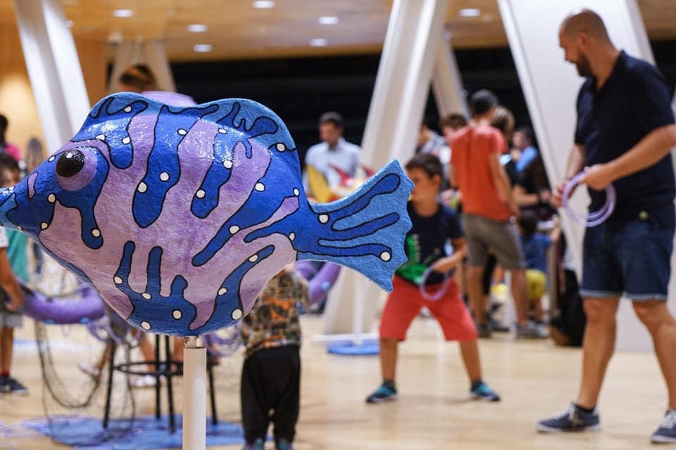 Several people enjoy an exhibit featuring a large purple and blue fish at the CosmoCaixa.