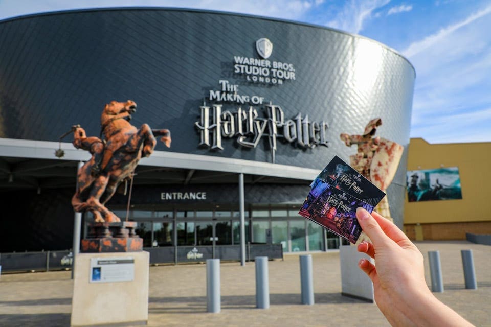 A hand holding a ticket in front of Warner Bros Studio near London.