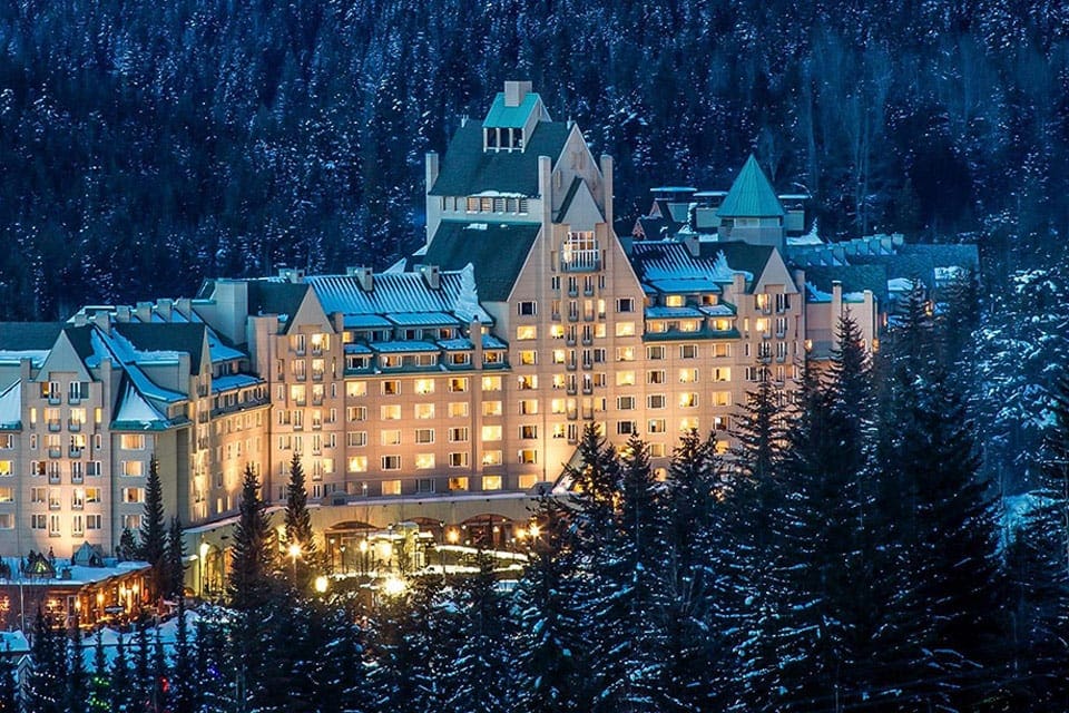 Fairmont Château Whistler at night during the winter, showered in bright lights.
