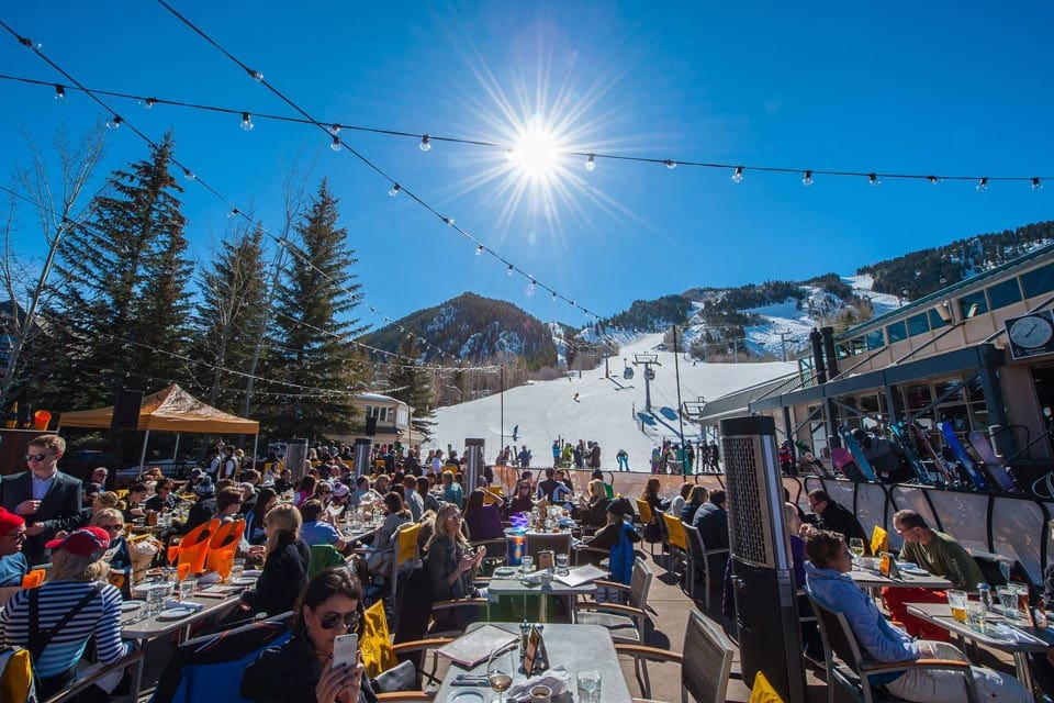 Several people eat at picnic tables while skiing on a winter day at The Little Nell