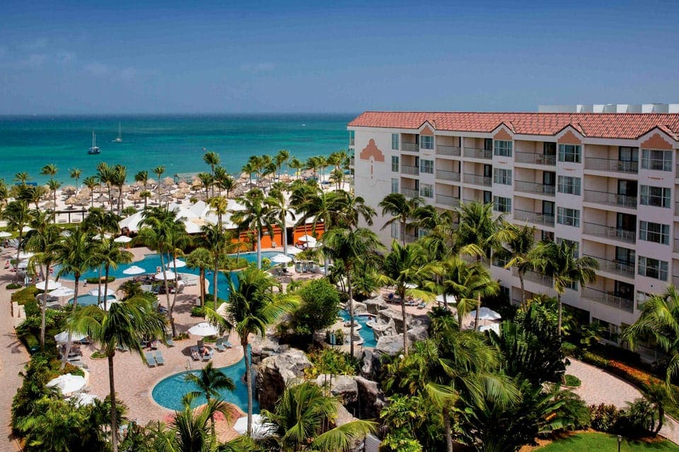 An aerial view of Aruba Marriott Ocean Club, one of the best family resorts in Aruba, featuring palm trees, large buildings, and a pool.