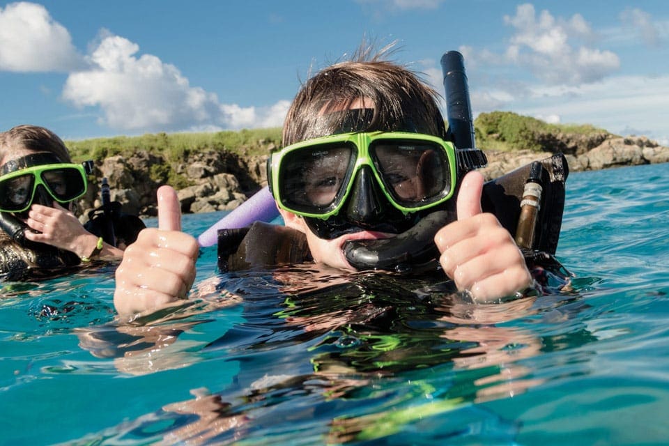 A child wearing snorkeling gear gives two thumbs up while swimming at Aruba Marriott Ocean Club.