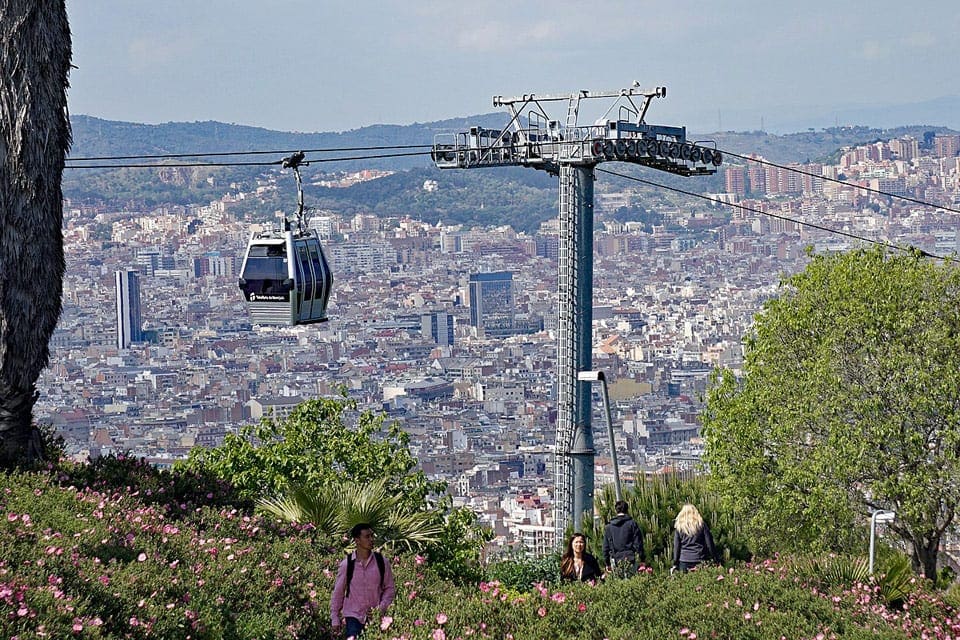 A view of the Montjuic Cable Car overhead, while a man wearing purple strolls through a Barcelona street.
