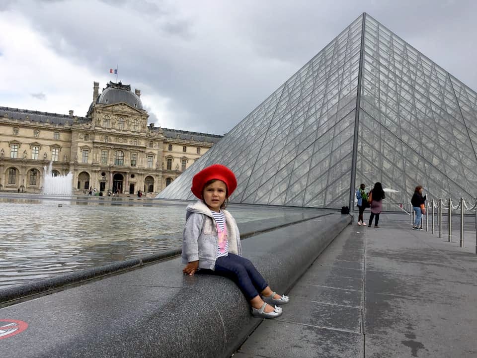 A kid sitting in front of the Louvre in Paris, France.