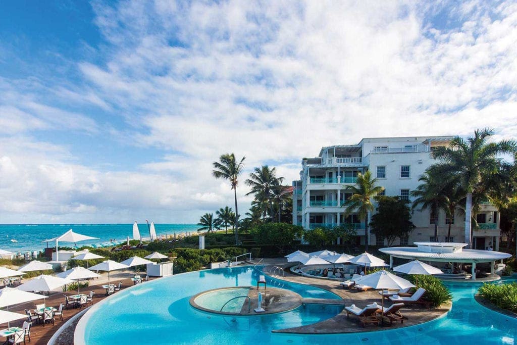 The epic pool at The Palms Turks and Caicos, with resort buildings in the background and beach access on the left.