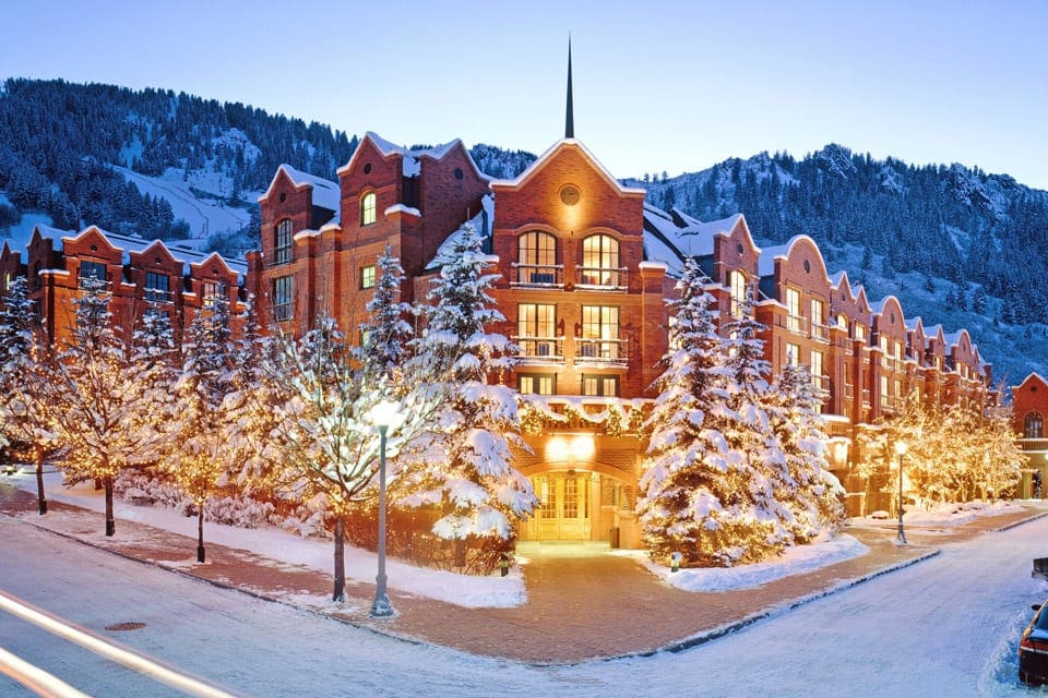 The corner entrance to St. Regis Aspen Resort on a snowy night, the hotel seems to glow in the winter night, one of the best places to stay when visiting Aspen during the winter with kids.