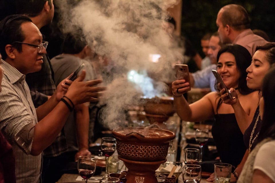 Please inside The Traveler’s Table taking pictures of a large cauldron emitting food smoke.