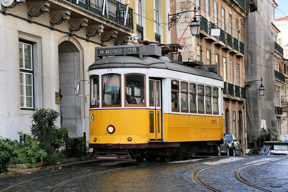 Tram 28, a yellow tram, races down a line in the city center of Lisbon. Learning about transportation is important in learning all about Lisbon with kids.