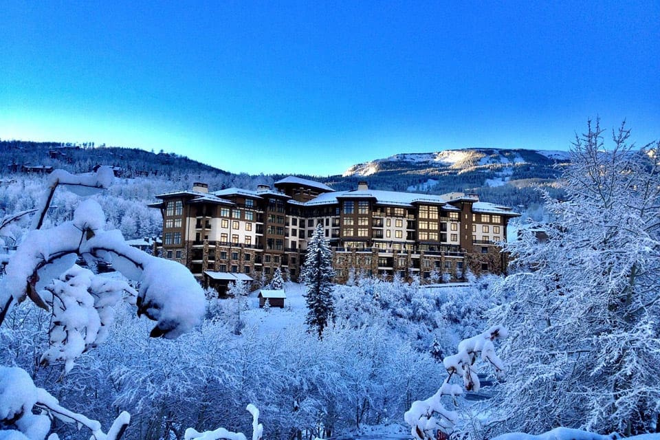 Through snowy trees, Viceroy Snowmass sits proudly amongst the mountains lit up at night.