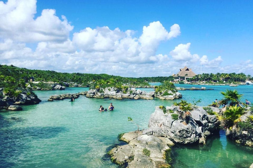 An expansive view of Xel-Há Park, featuring calm waters, rock formations, and a few swimmers.