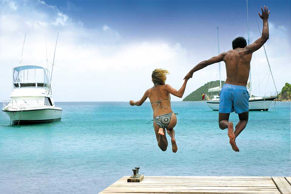 A dad and his young son jump from a boardwalk deck at Curtain Bluff, with boats in the distance.
