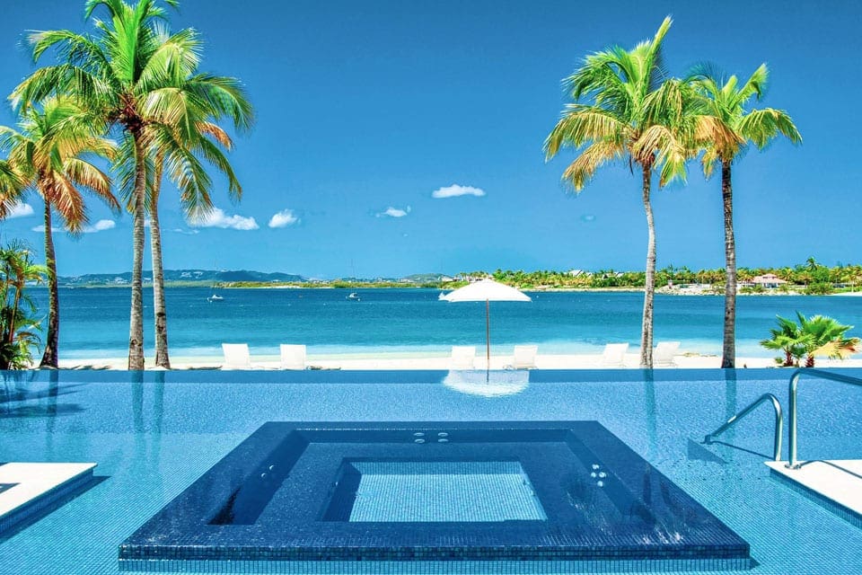 The tranquil, blue pool with the ocean in the distance at The Jumby Bay Island Resort, one of the best all-inclusive resorts in the Caribbean for families.