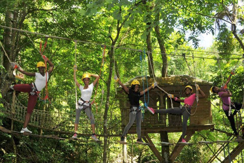 Several kids walk along a bridge in the canopy while zip-lining, , one of the best things to do in Antigua with kids.