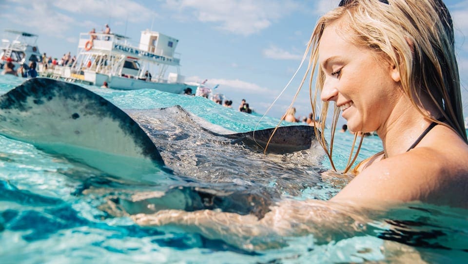 A woman smiles down looking at a sting ray in the water off the coast of the Kimpton Seafire Resort + Spa in Grand Cayman.