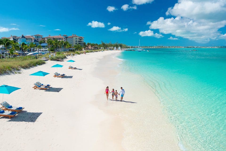 Aerial view of a family of four walking alonge a pristine beach at Beaches Turks & Caicos, one of the best Caribbean resorts with baby clubs.